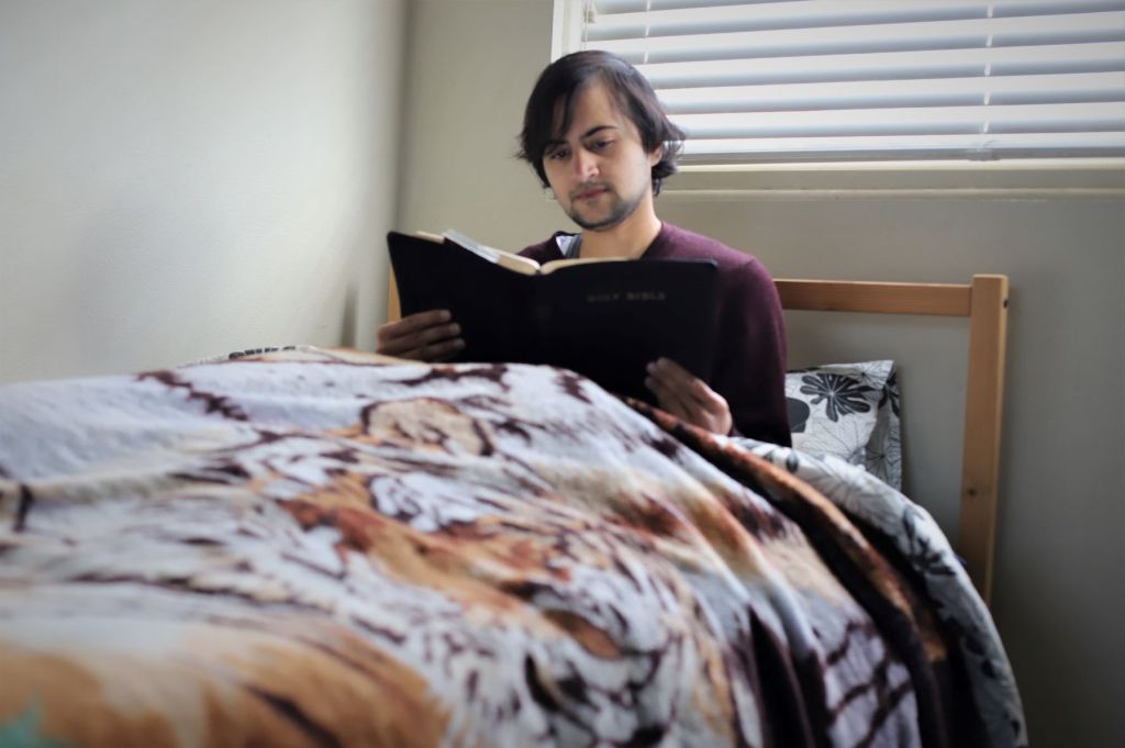 A woman sits up in bed reading a Bible.